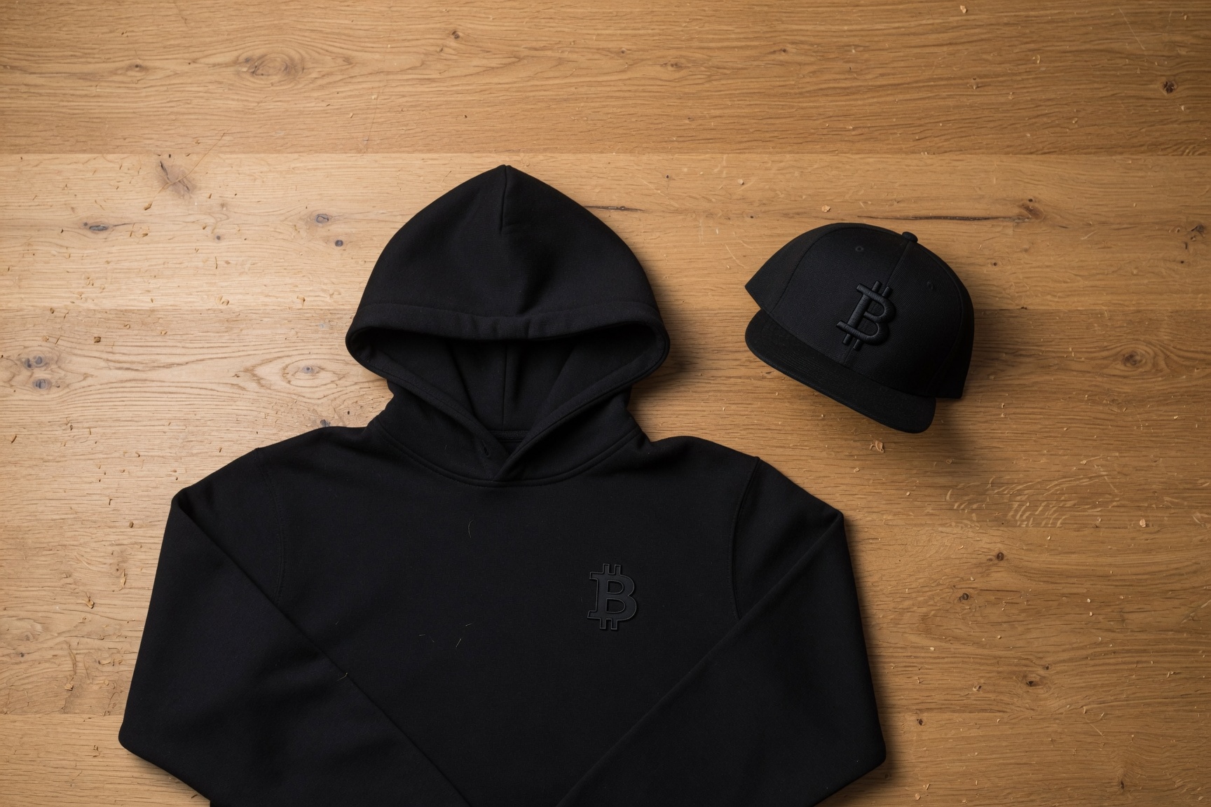 Bitcoin hoodie and snapback cap flat lay on oak surface